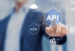 A person in a suit points at a transparent screen displaying the word &ldquo;API&rdquo; and various technology icons, including a cloud, gears, a smartphone, and code symbols, representing application programming interfaces.